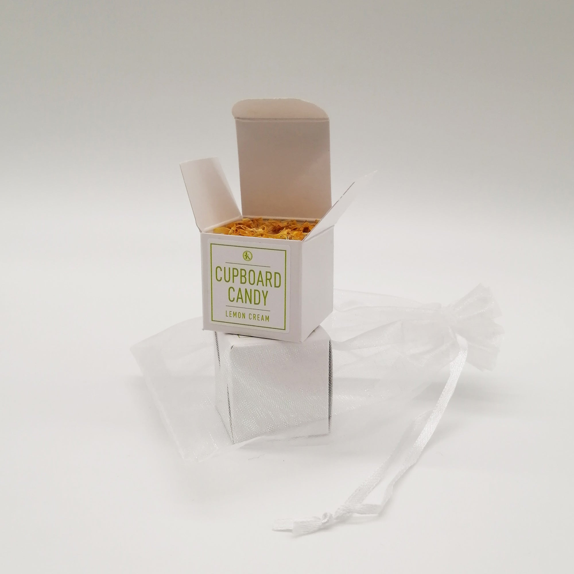 A small, neatly packaged box labeled 'CUPBOARD CANDY' with a green icon, alongside an organza bag. The box is white with a minimalistic design.