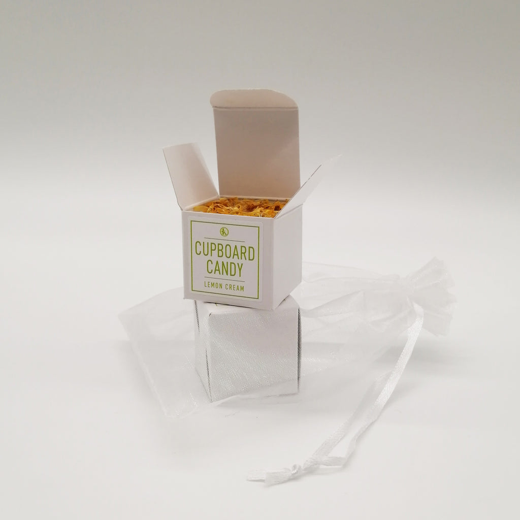 A small, neatly packaged box labeled 'CUPBOARD CANDY' with a green icon, alongside an organza bag. The box is white with a minimalistic design.