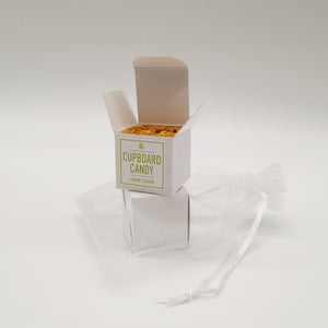 A small, neatly packaged box labeled 'CUPBOARD CANDY' with a green icon, alongside an organza bag. The box is white with a minimalistic design.