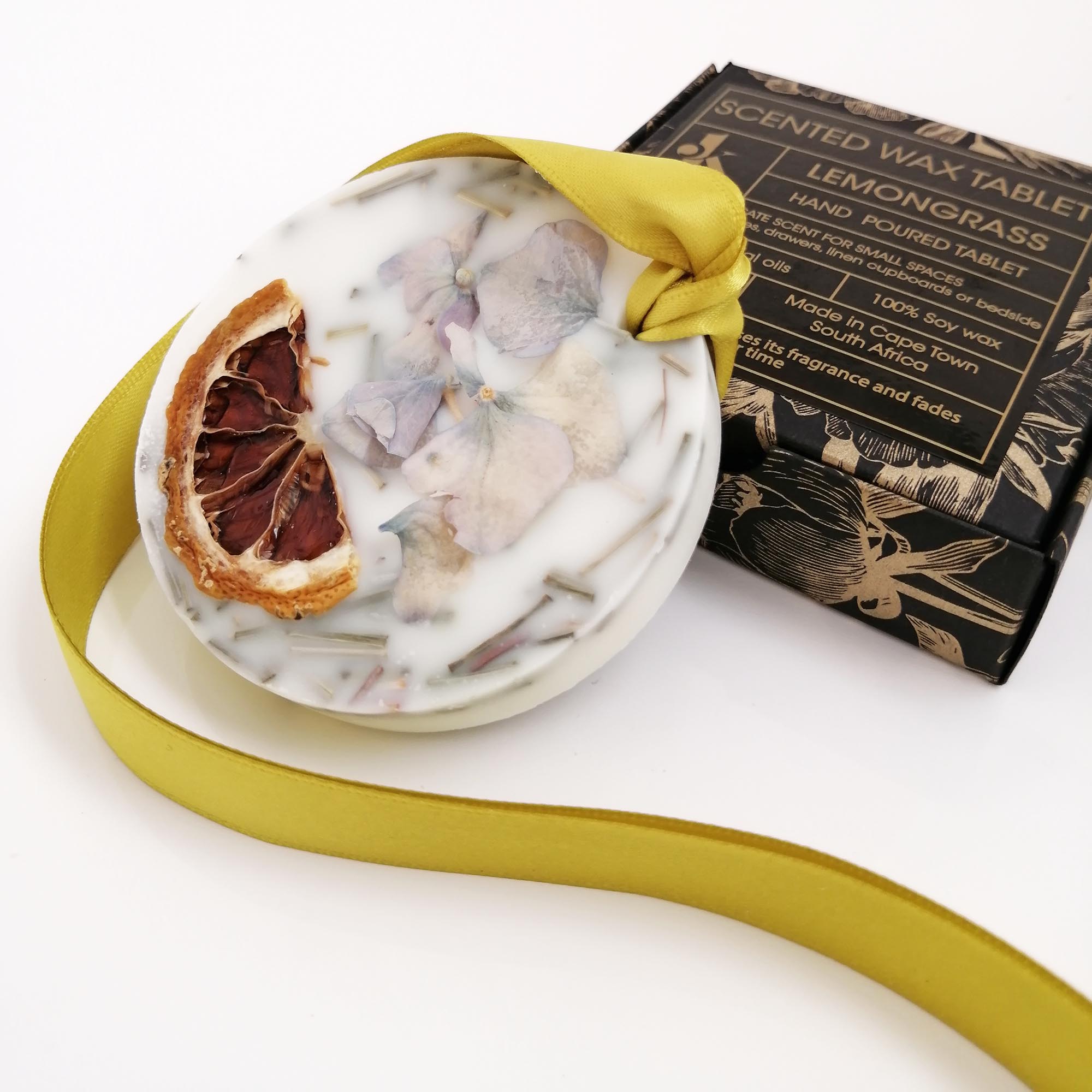 Decorative wax tablet with citrus peel and a yellow ribbon, with a box labeled 'Scented Wax Tablet Lemongrass' in the background.