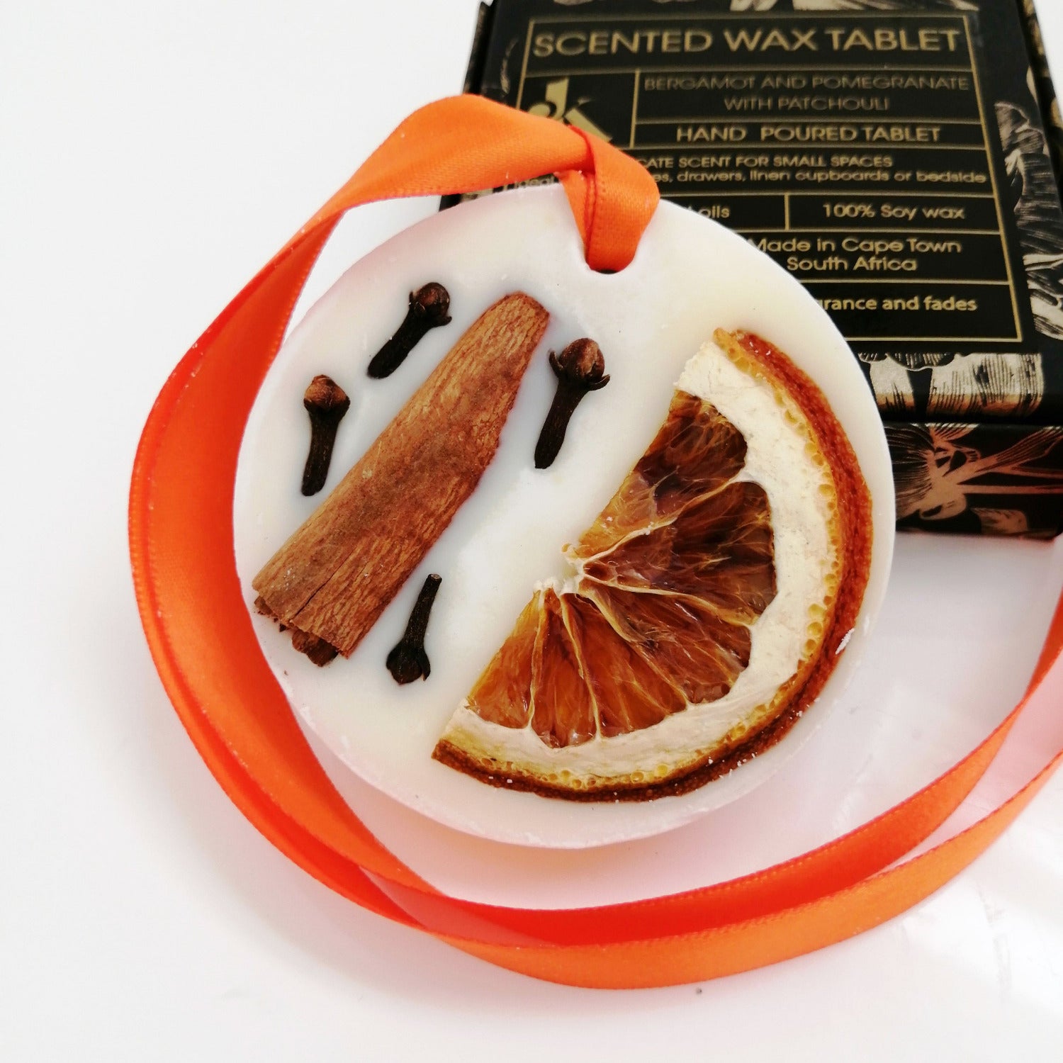 Decorative wax tablet with citrus peel petals and an orange ribbon, with a box labeled 'Scented Wax Tablet Spicy Orange' in the background.