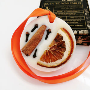 Decorative wax tablet with citrus peel petals and an orange ribbon, with a box labeled 'Scented Wax Tablet Spicy Orange' in the background.