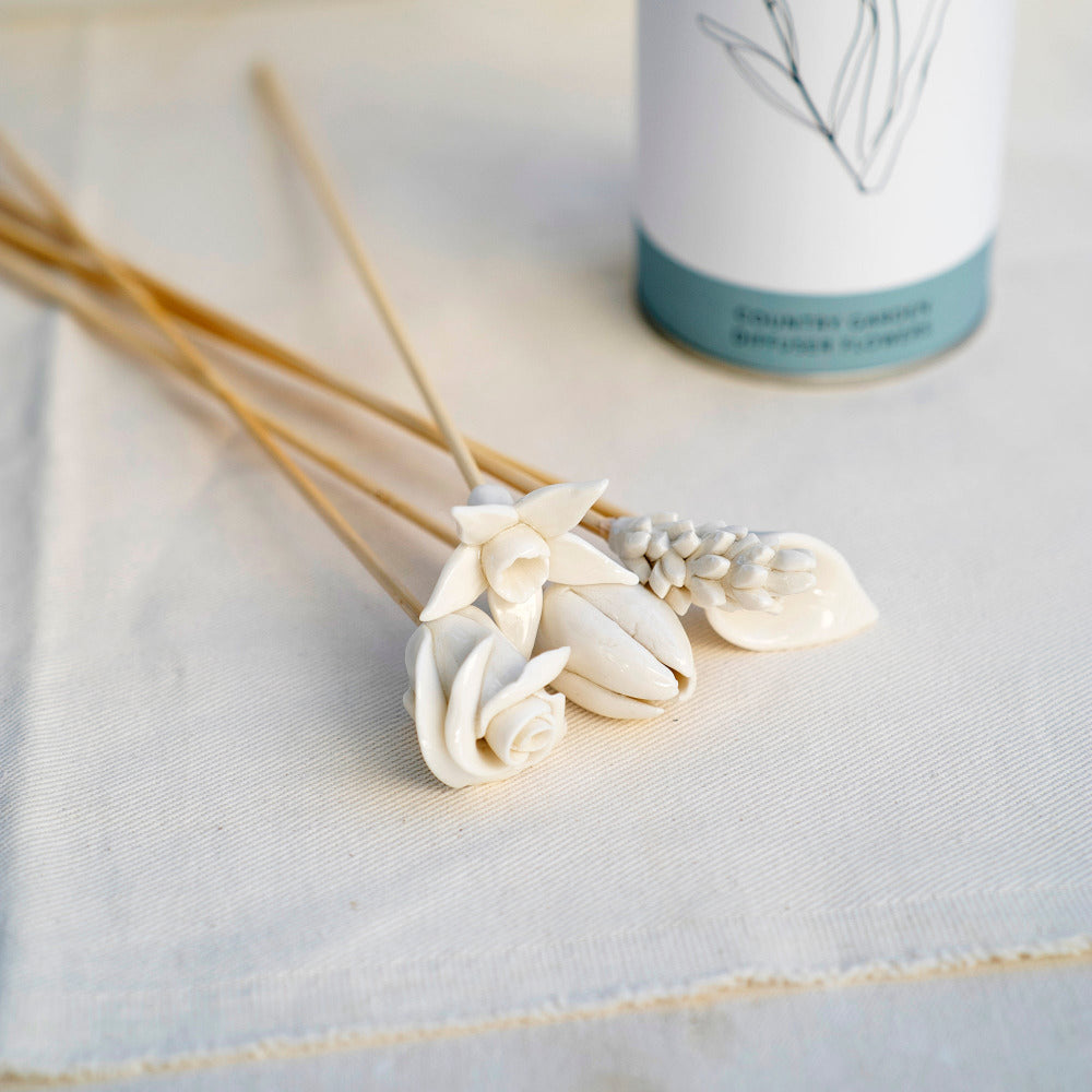 Decorative reed diffusers with porcelain floral toppers on bamboo sticks on a light fabric background
