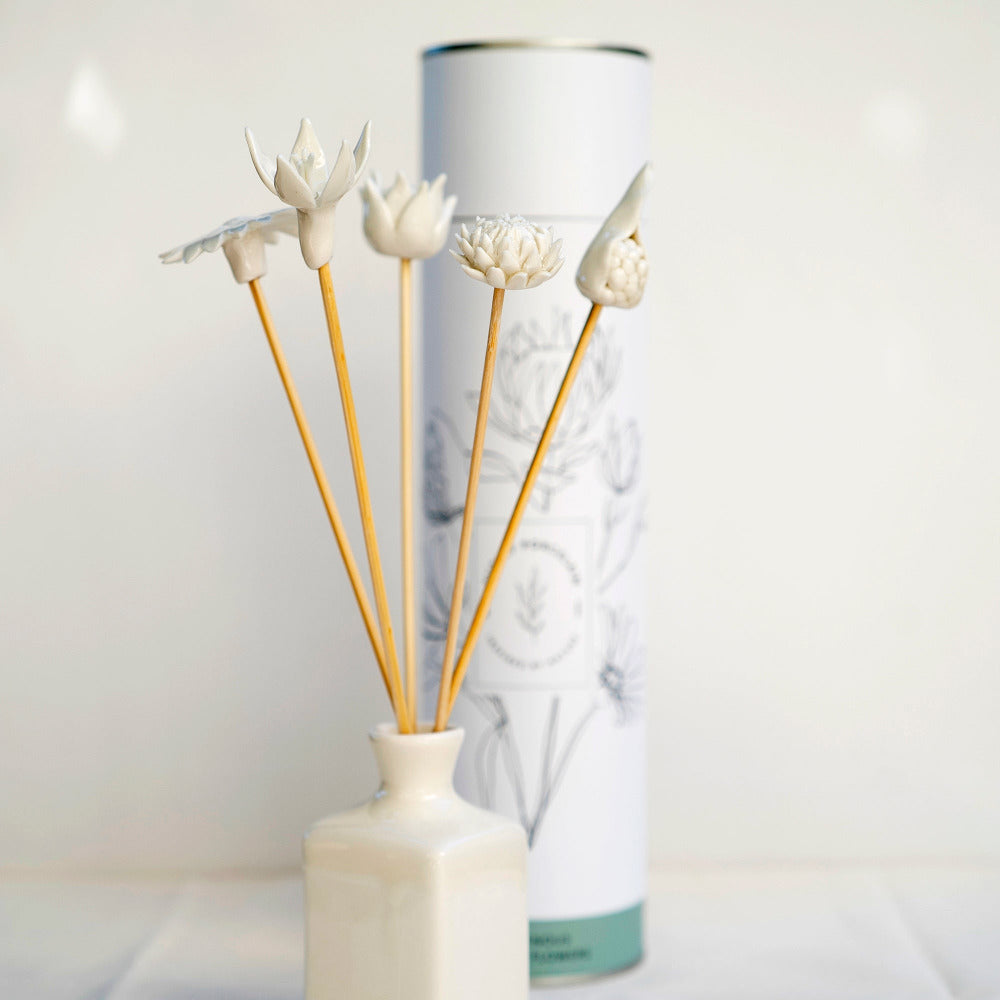 A set of handcrafted porcelain diffuser sticks with various floral designs placed in a white vase, with a cylindrical container in the background.