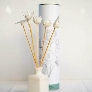 A set of handcrafted porcelain diffuser sticks with various floral designs placed in a white vase, with a cylindrical container in the background.