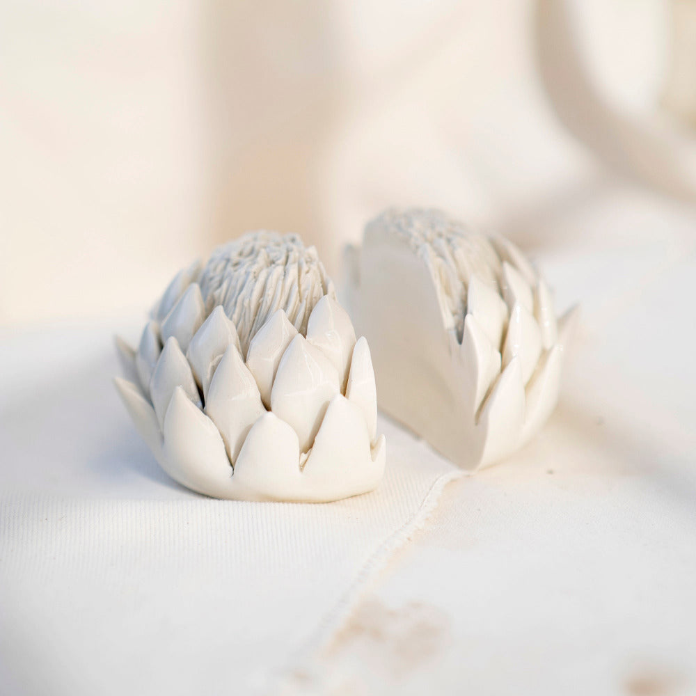 Two porcelain bookends in the shape of half a king protea flower each displayed on a textural white background.