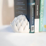 Load image into Gallery viewer, A porcelain bookend in the shape of a half of a king protea holding up a number of books.
