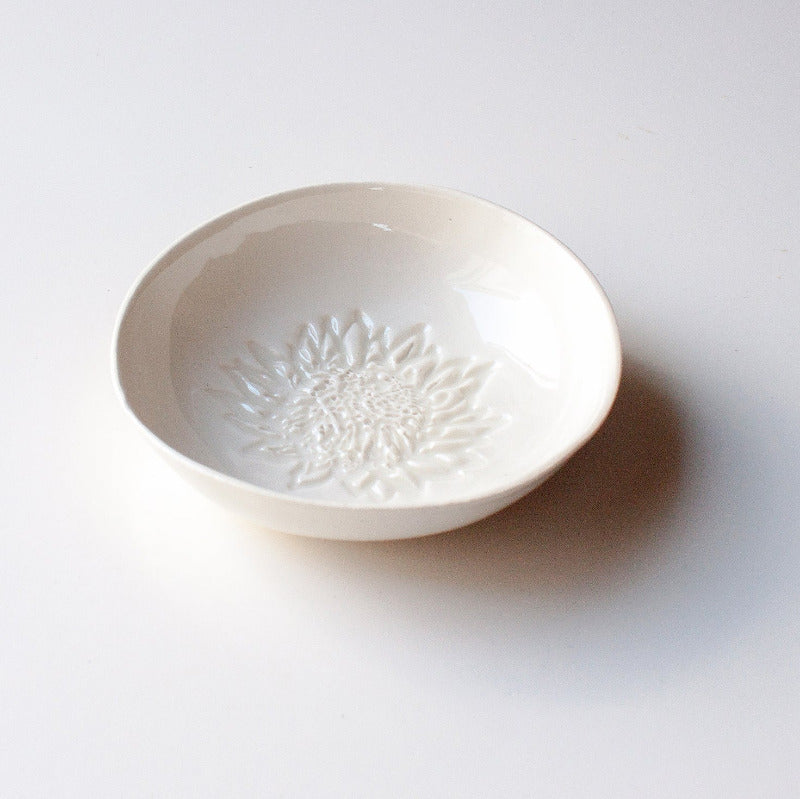 A white porcelain dipping bowl with a king protea silhouette stamped into the base. 