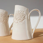 Load image into Gallery viewer, Two white ceramic jugs with protea patterns, placed on a wooden surface against a white background.
