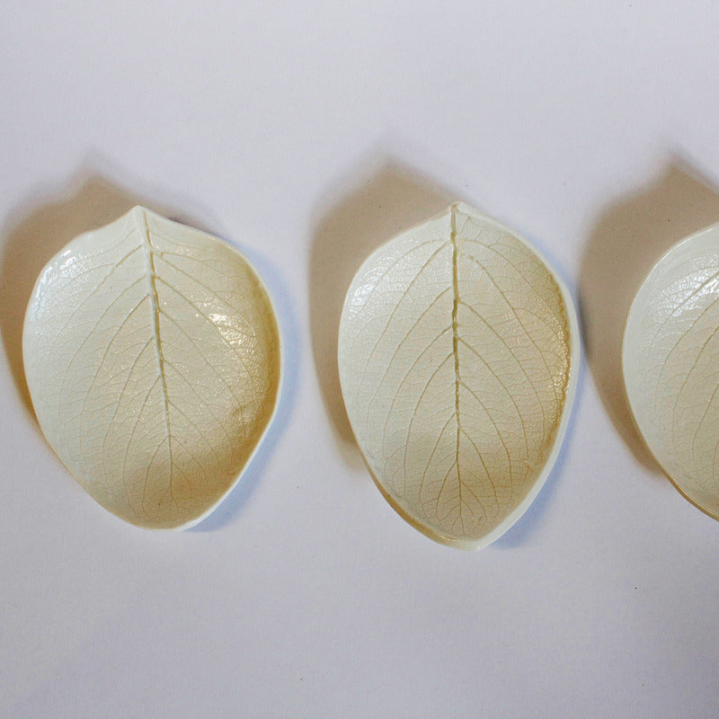 A top down photograph of white porcelain soap dishes in the shape of leaves with the leaf veins and details pressed into the ceramic. 