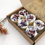 Load image into Gallery viewer, A box of 12 white soy wax melts with multicolored floral toppings, placed in a cardboard box with a floral design. Some dried flowers are also visible to the side.
