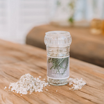 Load image into Gallery viewer, A clear glass culinary grinder labeled &#39;Rhino Bush&#39; with visible white salt crystals next to it on a wooden surface.
