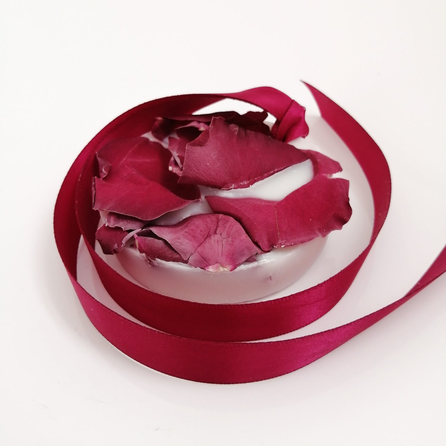 A wax tablet with a rose and geranium scent, featuring a pink ribbon design, partially melted with rose petals scattered on top.