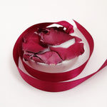 Load image into Gallery viewer, A wax tablet with a rose and geranium scent, featuring a pink ribbon design, partially melted with rose petals scattered on top.
