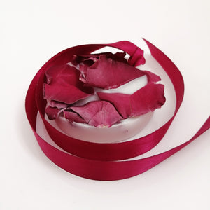 A wax tablet with a rose and geranium scent, featuring a pink ribbon design, partially melted with rose petals scattered on top.