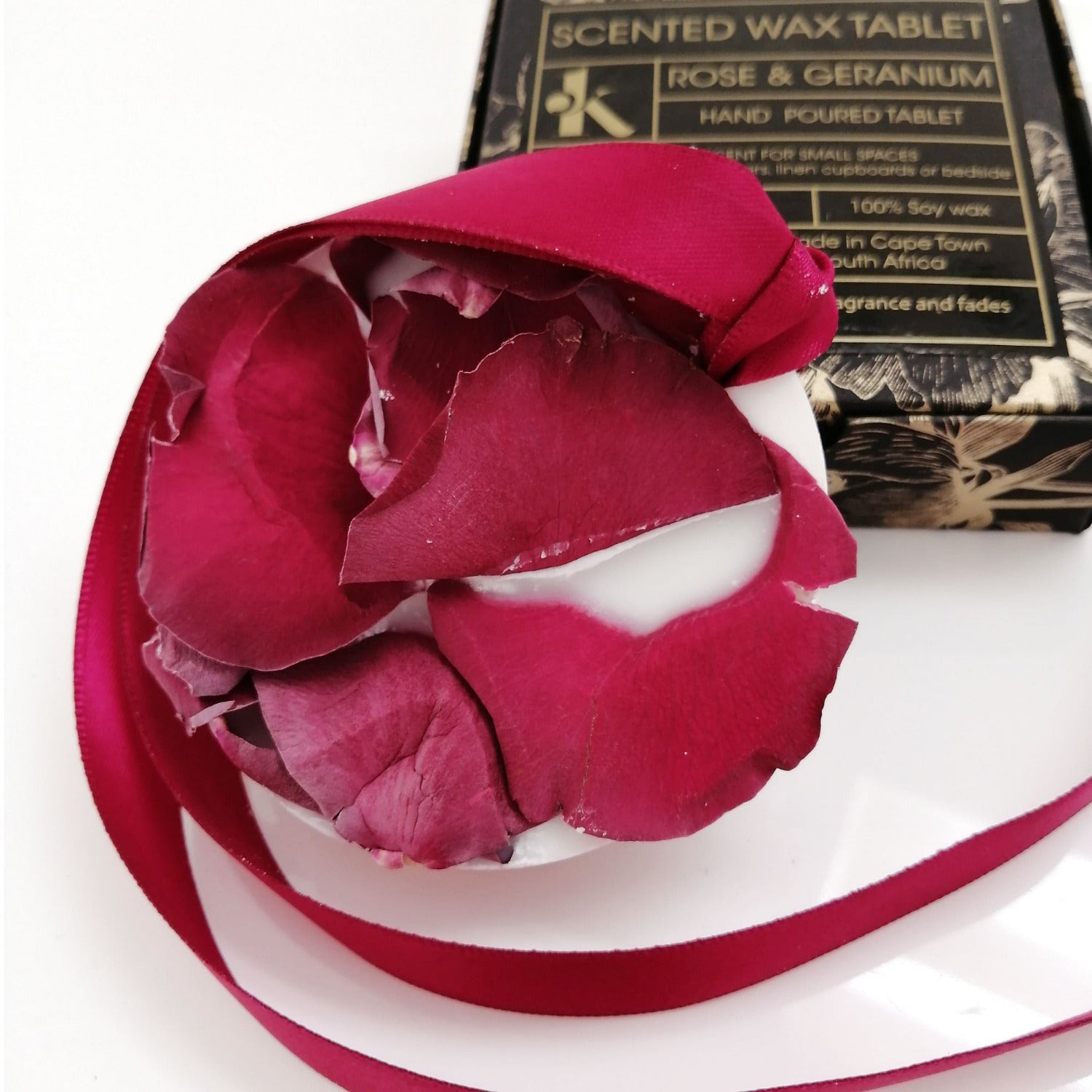 Scented wax tablet with rose and geranium fragrance on a white base with packaging in the background
