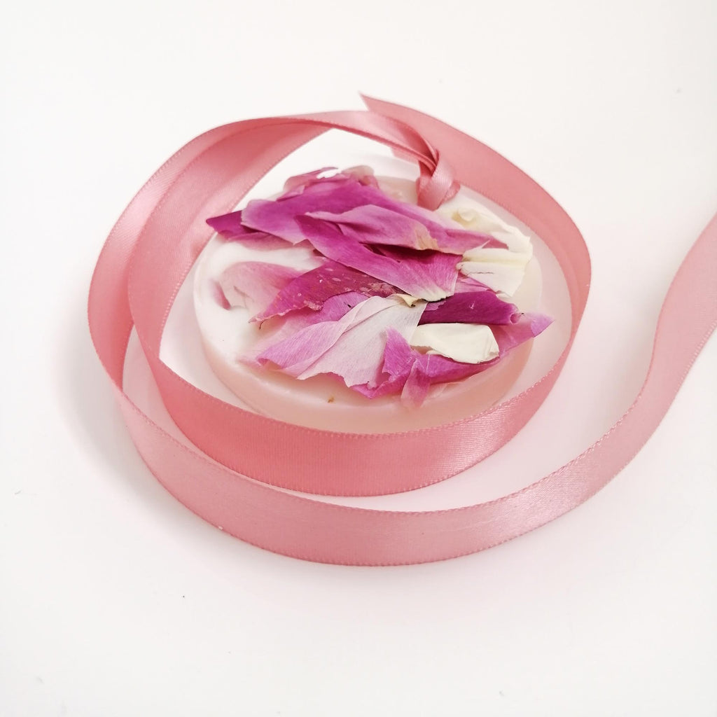 A wax tablet with a wild rose scent, adorned with pink ribbon and rose petals, set on a white background.